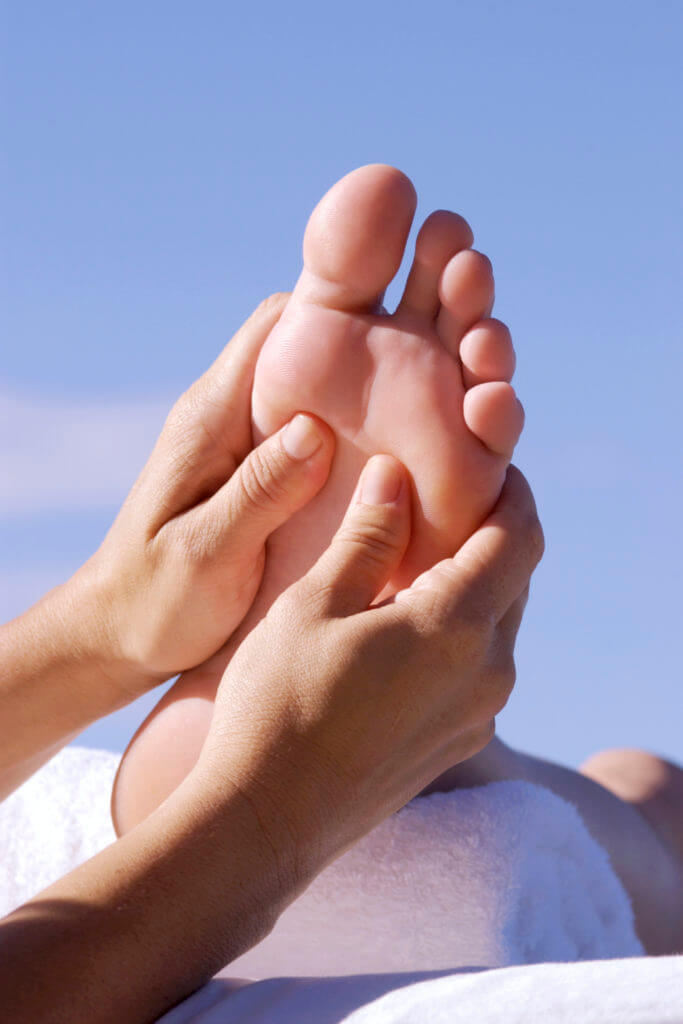 Reflexology and its results; picture of two hands holding the bottom of a foot with a blue sky in the background