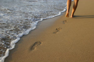 emotional healing power of reflexology; foot prints in the sand with water on the beach